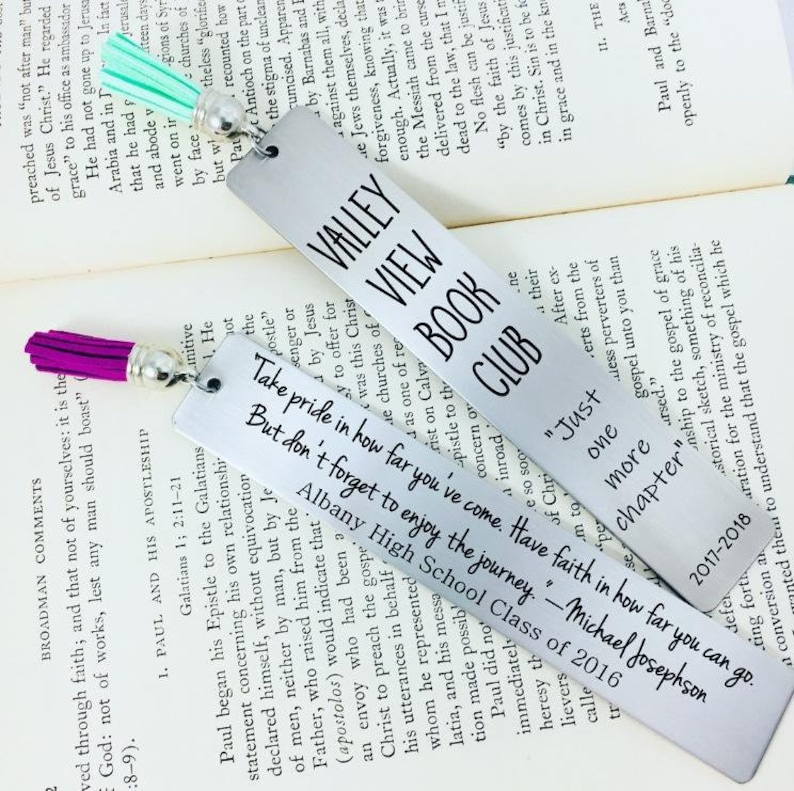 Design your own engraved metal bookmark with laser etched text, custom fonts, and colorful tassels. Stainless steel personalized bookmarks shown in lifestyle setting emphasize clean engraving detail and durable construction ideal for reader gifts and literary keepsakes.