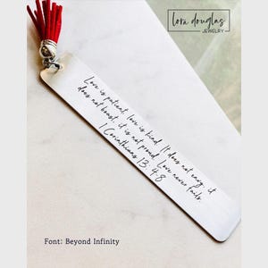 May include: A rectangular silver-toned metal bookmark featuring the engraved text Love is patient, love is kind. It does not envy, it does not boast, it is not proud. Love never fails. 1 Corinthians 13: 4-8. A bright red tassel is attached to the top.