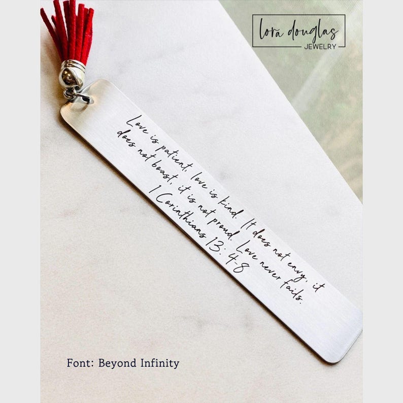 May include: A rectangular silver-toned metal bookmark featuring the engraved text Love is patient, love is kind. It does not envy, it does not boast, it is not proud. Love never fails. 1 Corinthians 13: 4-8. A bright red tassel is attached to the top.