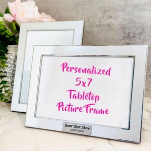 Peut inclure: Cadre photo de table en argent avec un passe-partout blanc et une inscription personnalisée. Le cadre mesure 12,7 x 17,8 cm et comporte une plaque argentée en bas avec le texte "Your Text Here and here".
