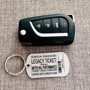 K&ouml;nnte beinhalten: Ein silberner Schl&uuml;sselanh&auml;nger aus Metall mit einem Schl&uuml;sselring und einem Anh&auml;nger, auf dem "DSOA DANCE LEGACY TICKET FOR ALL MEYER HALL PERFORMANCES TICKET VALID FOREVER GIVEN WITH GRATITUDE" und "ADMIT TWO" auf der rechten Seite steht.