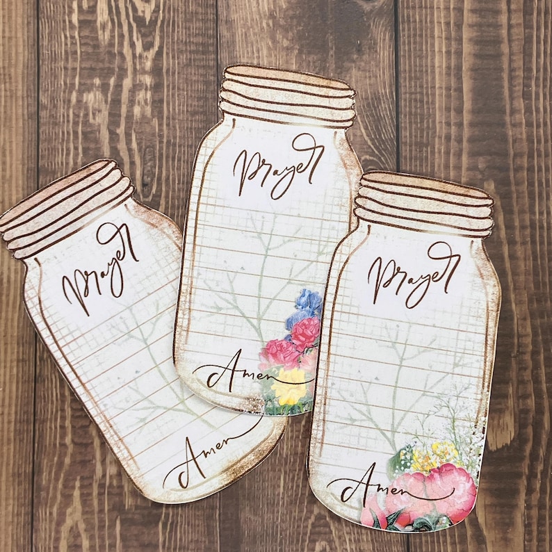 Op de afbeelding: Drie uitgestanste papieren kaarten in de vorm van weckpotten met een ruitjesachtergrond. Elke kaart heeft het woord Prayer in bruin handschrift bovenaan en Amen onderaan. Florale illustraties in roze, blauw en geel sieren de potten.