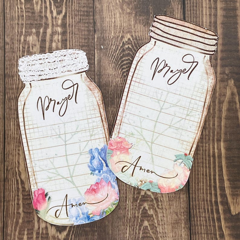 Op de afbeelding: Twee platte, inmaakpotvormige papieren kaarten met een rasterachtergrond, het woord Prayer bovenaan en het woord Amen onderaan. De ontwerpen bevatten florale illustraties in aquarel-stijl in roze en blauw, waarbij &eacute;&eacute;n pot een deksel met een wit kantpatroon heeft.