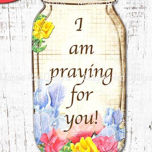 Op de afbeelding: Een kaart in de vorm van een weckpot met een rasterachtergrond en de tekst I am praying for you! in bruin schrift. Het ontwerp is versierd met aquarelachtige illustraties van gele, blauwe en roze bloemen aan de boven- en onderranden.
