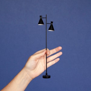 May include: A black metal floor lamp with two black cone-shaped lampshades. The lamp is being held in a person's hand.
