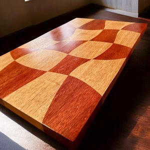 May include: A wooden coffee table with a checkerboard pattern in shades of reddish-brown and light brown. The table has a curved, wave-like design in the center. The table is approximately 48 inches long and 24 inches wide.