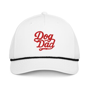 May include: White baseball cap featuring the red embroidered text "Dog Dad". The cap has a black rope detail around the brim and a curved visor. A fashionable accessory for dog lovers.