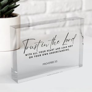 May include: A clear acrylic block with the text "Trust in the Lord" in elegant script. The block also includes the scripture "Proverbs 3:5". A potted succulent plant sits in the background.
