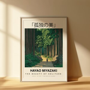 May include: Framed art print featuring a serene forest path scene. The artwork includes the Japanese text "孤独の美" and the English text "HAYAO MIYAZAKI THE BEAUTY OF SOLITUDE". The image depicts a person walking on a path surrounded by tall trees.