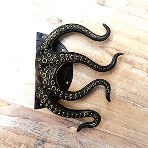 May include: Black octopus door knocker with gold accents. The octopus has eight tentacles and is mounted on a round black base.