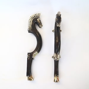 May include: A pair of black and gold horse head door handles. The handles are made of metal and have a detailed design.