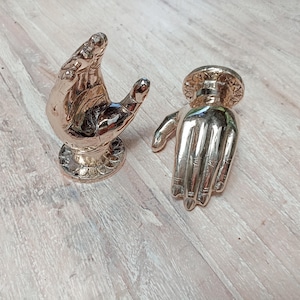 Puede incluir: Dos tiradores de puerta de metal dorado en forma de manos. Los tiradores están detallados con diseños intrincados y tienen un acabado pulido.