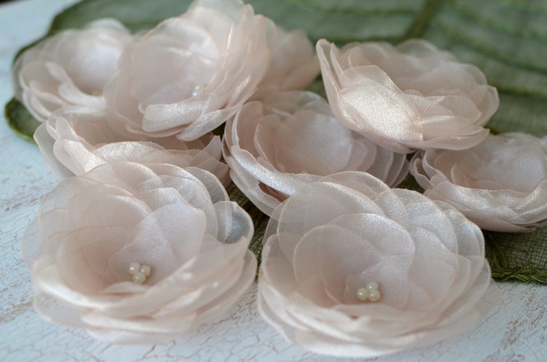 May include: A group of eight blush pink silk flowers with pearl centers. The flowers are layered and have a delicate, romantic look.