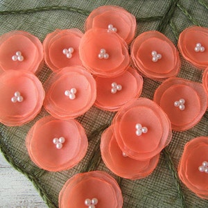 May include: A collection of peach-coloured fabric flowers with pearl accents. The flowers are layered and have a delicate, ruffled appearance.