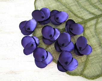 May include: Purple fabric flower embellishments with black centers. The flowers are arranged on a green textured surface.