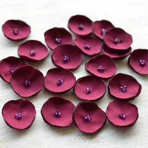 May include: A collection of burgundy fabric flower petals with purple bead centres.