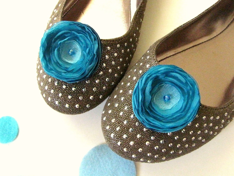 Puede incluir: Un par de pisos marrones con un acabado brillante y una flor de tela azul turquesa como adorno en cada zapato.