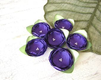May include: Six purple fabric flowers with green leaves. Each flower has a pearl center.