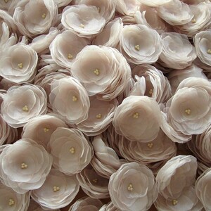 May include: A collection of delicate, pale pink fabric flowers. The flowers are made of multiple layers of sheer fabric, creating a soft and romantic look.