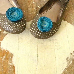 Puede incluir: Un par de pisos marrones con lunares blancos y un adorno de flor turquesa en cada zapato.