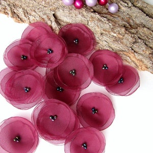May include: Burgundy red fabric flower embellishments with black bead centers. The flowers are layered and have a delicate, ruffled texture.