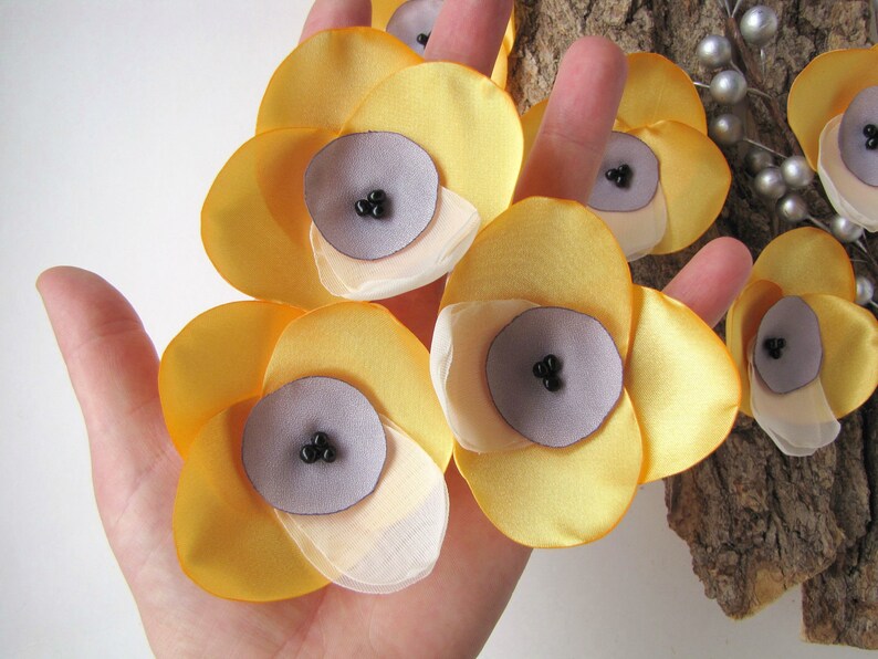 May include: Five yellow fabric flowers with a layered design. Each flower has a center made of a light purple fabric with three black beads.