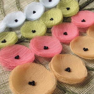 Peut inclure: Une décoration murale faite de fleurs en tissu superposées dans des tons de rose, pêche, jaune, vert et bleu. Chaque fleur a un centre de perles noires.