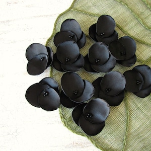 May include: A collection of black satin flower petals with black bead centres. The petals are arranged in a cluster on a green background.