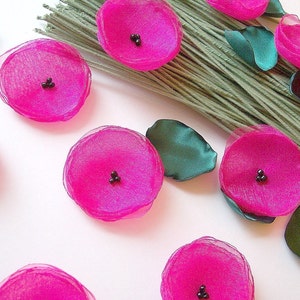 May include: A set of pink fabric flowers with black centers. The flowers are arranged on a white surface.