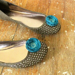 Puede incluir: Un par de pisos marrones brillantes con un adorno de flor turquesa en cada dedo del pie.