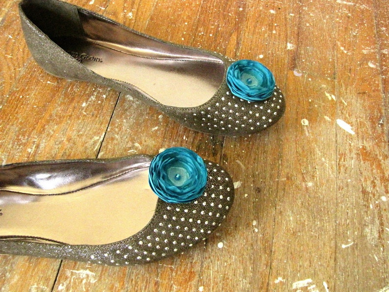 Puede incluir: Un par de pisos marrones brillantes con un adorno de flor turquesa en cada dedo del pie.