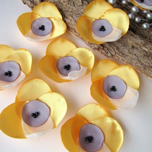 May include: Seven yellow fabric flowers with a layered design. Each flower has a center made of a light purple fabric with a darker purple center.