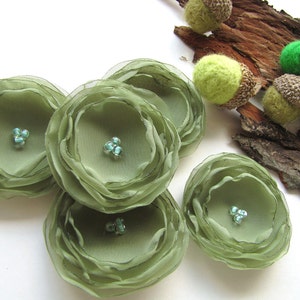 May include: Five green fabric flowers with a layered, ruffled design. Each flower has three small, turquoise-colored beads in the center.
