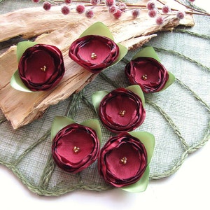 May include: Six burgundy fabric flowers with green leaves. Each flower has a centre made of gold beads.