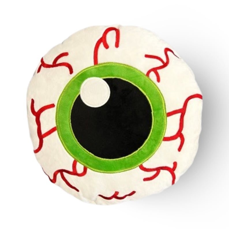 May include: A white plush pillow shaped like a large eyeball with a green iris and black pupil. Red veins are embroidered around the eye.
