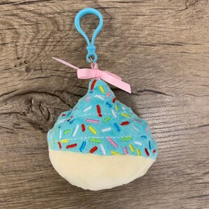 May include: A blue and white cupcake-shaped plush keychain with pink ribbon and a blue plastic clip.