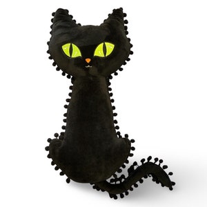 May include: Black plush cat with green eyes and a black pom-pom trim. The cat is sitting with its tail curled around its body.