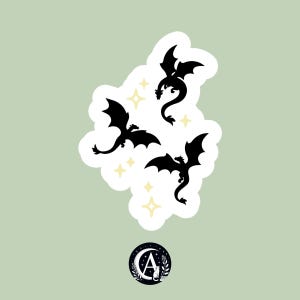 Könnte beinhalten: Ein Aufkleber mit drei schwarzen Drachensilhouetten mit ausgebreiteten Flügeln, angeordnet auf einem weißen, wolkenförmigen Hintergrund. Das Design umfasst gelbe Sternakzente und ein kreisförmiges Logo mit Mond und Katze.
