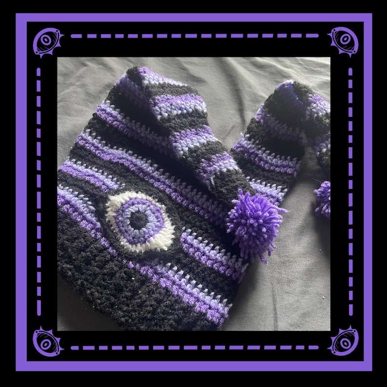 May include: A handmade crochet hat in black, purple, and white. The hat features a large eye design on the front and a pom-pom. The hat is a unique accessory, perfect for adding a touch of whimsy to any outfit.