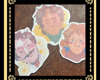 May include: Three die-cut stickers featuring illustrated portraits. One has a mustache and star, another has hearts, and the third has curly hair. Each portrait is surrounded by a floral design, with a brown wooden background.