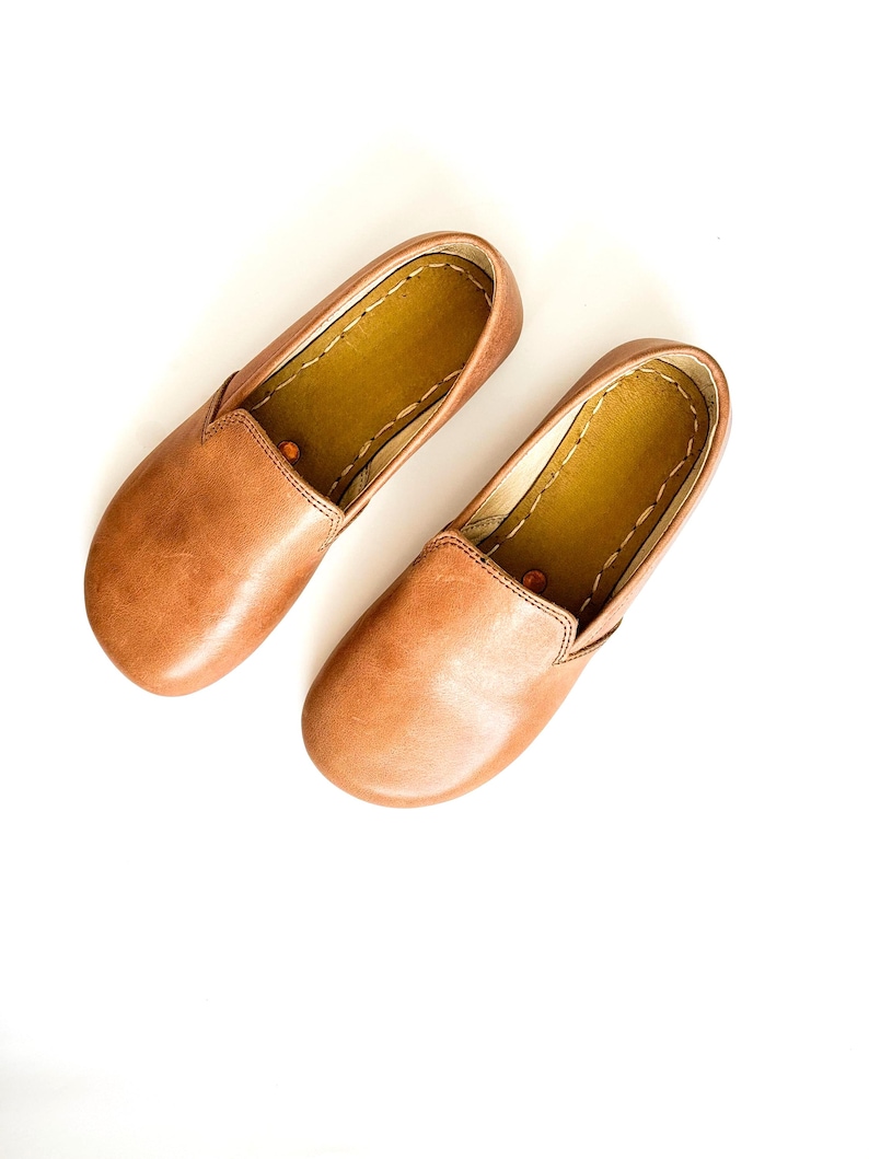 Pode incluir: Um par de sapatos slip-on de couro castanho. Os sapatos t&ecirc;m bico arredondado e perfil baixo. O interior &eacute; castanho mais claro, com costuras vis&iacute;veis nas bordas. Sapatos confort&aacute;veis para uso di&aacute;rio.