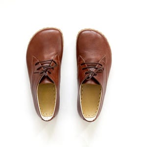Peut inclure: Paire de chaussures en cuir marron avec lacets, sur fond blanc. Les chaussures ont un bout arrondi et un int&eacute;rieur de couleur claire. Le cuir semble lisse et les lacets sont marron fonc&eacute;. Chaussures pour tous les jours.