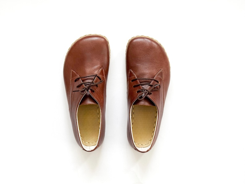 Peut inclure: Paire de chaussures en cuir marron avec lacets, sur fond blanc. Les chaussures ont un bout arrondi et un int&eacute;rieur de couleur claire. Le cuir semble lisse et les lacets sont marron fonc&eacute;. Chaussures pour tous les jours.