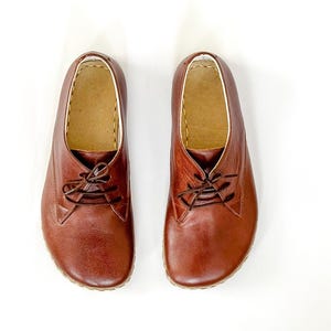 Peut inclure: Une paire de chaussures &agrave; lacets en cuir marron. Les chaussures ont un bout arrondi et une semelle de couleur claire. L'int&eacute;rieur est de couleur beige clair et les coutures sont visibles sur les bords. Les chaussures sont pr&eacute;sent&eacute;es sur fond blanc.