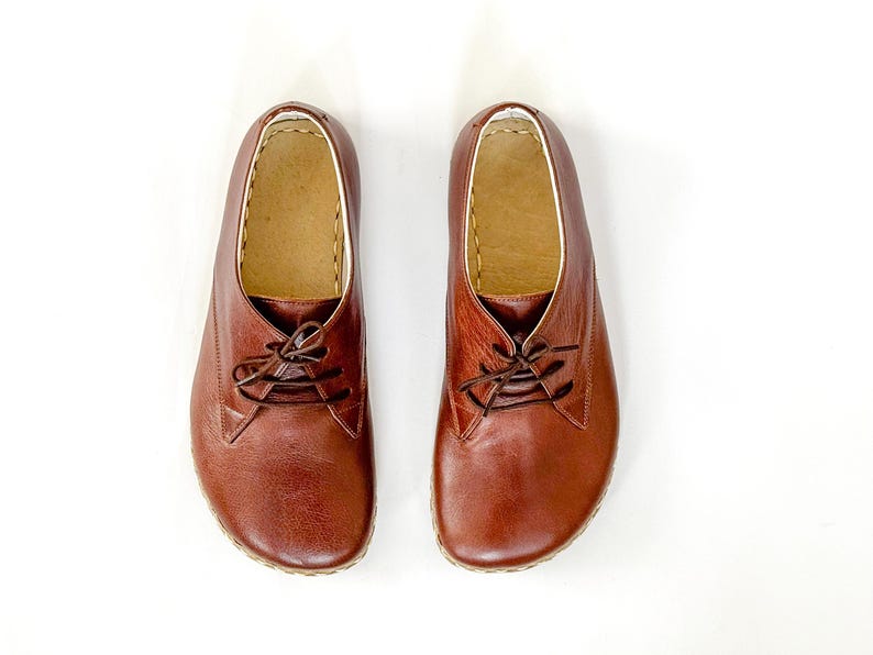 Peut inclure: Une paire de chaussures &agrave; lacets en cuir marron. Les chaussures ont un bout arrondi et une semelle de couleur claire. L'int&eacute;rieur est de couleur beige clair et les coutures sont visibles sur les bords. Les chaussures sont pr&eacute;sent&eacute;es sur fond blanc.