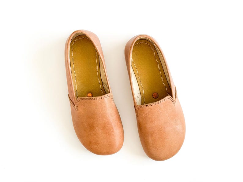 Pode incluir: Um par de sapatos slip-on de couro castanho claro. Os sapatos t&ecirc;m bico arredondado e perfil baixo. O interior &eacute; de cor castanho claro com costuras vis&iacute;veis. Sapatos novos e por usar, perfeitos para uso casual.
