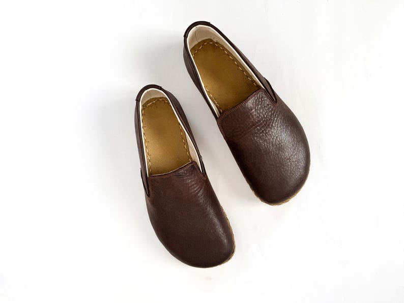 Pu&ograve; includere: Un paio di scarpe slip-on in pelle marrone. Le scarpe hanno una punta arrotondata e una superficie strutturata. L'interno &egrave; di un marrone pi&ugrave; chiaro e le scarpe sono su uno sfondo bianco. Le scarpe sembrano nuove.