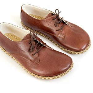 Peut inclure: Une paire de chaussures marron en cuir &agrave; lacets. Les chaussures ont un bout arrondi, une semelle cousue et des lacets marron. L'int&eacute;rieur est blanc et la semelle est de couleur beige clair. Les chaussures sont pr&eacute;sent&eacute;es sur fond blanc.