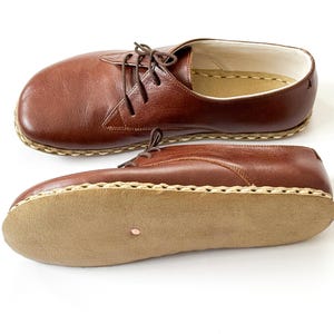 Peut inclure: Deux chaussures en cuir marron avec des lacets sont pr&eacute;sent&eacute;es sur fond blanc. Les chaussures ont un bout arrondi et une semelle cousue. La semelle est de couleur marron clair. Les chaussures sont de style classique.
