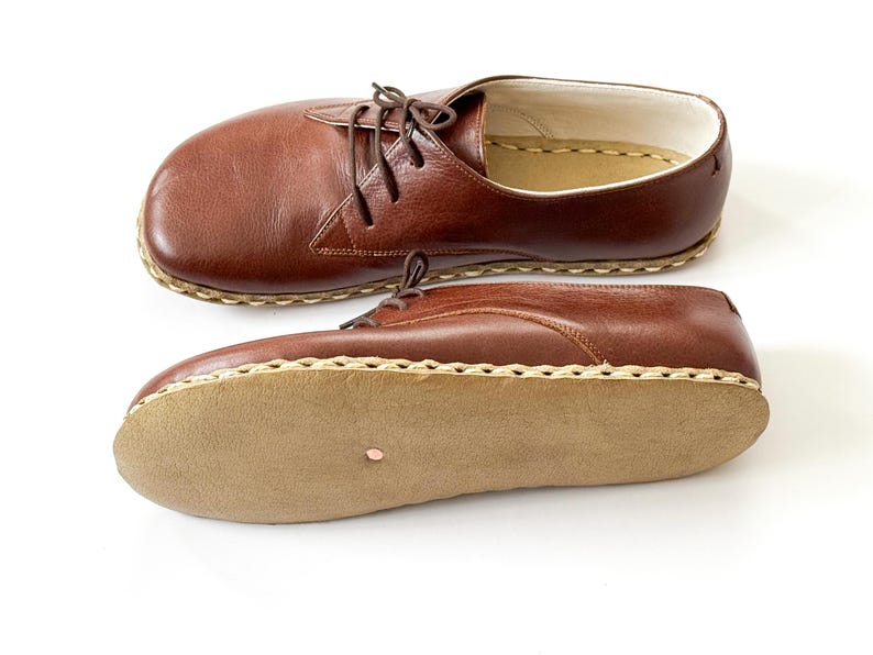 Peut inclure: Deux chaussures en cuir marron avec des lacets sont pr&eacute;sent&eacute;es sur fond blanc. Les chaussures ont un bout arrondi et une semelle cousue. La semelle est de couleur marron clair. Les chaussures sont de style classique.